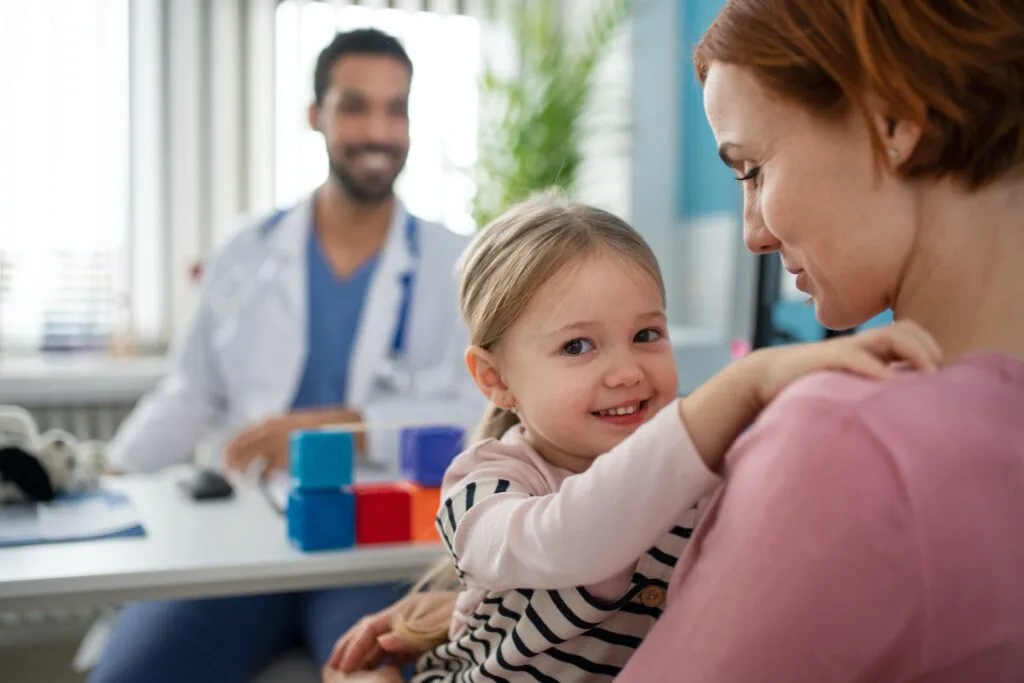 A smiling child sitting with an adult during a clinician visit